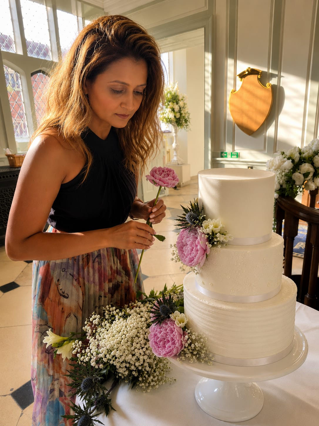 Baker adding fresh flowers to a white tiered wedding cake