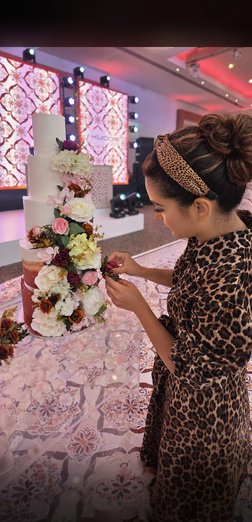Baker placing fresh flowers on a five-tier celebration cake at a venue
